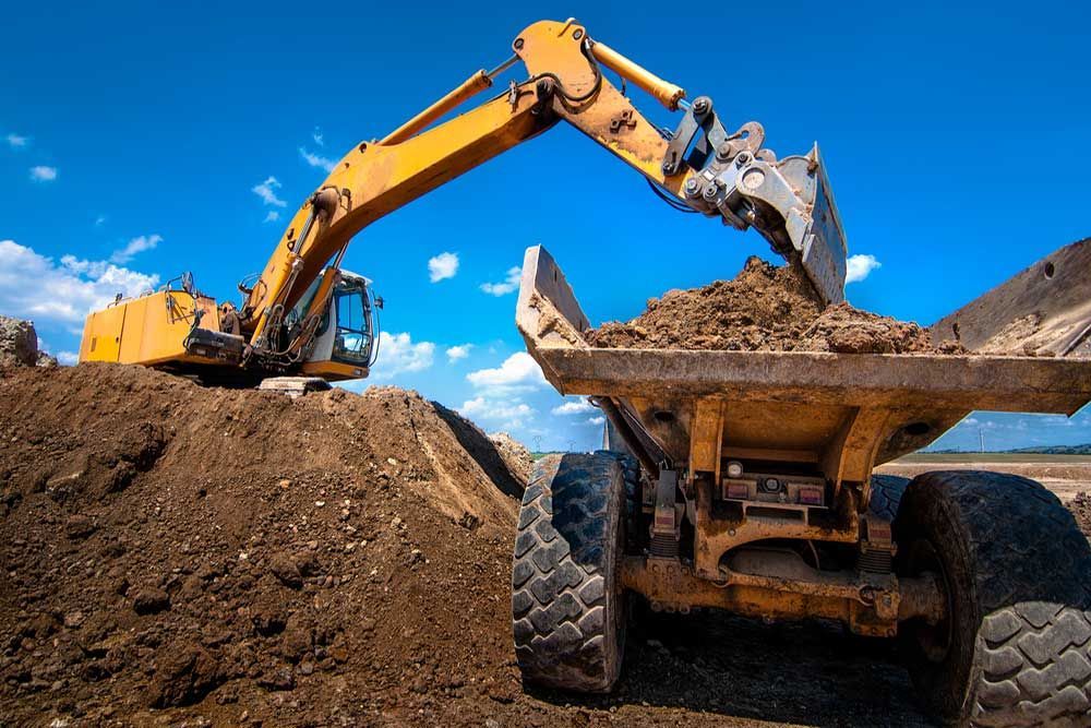A Yellow Excavator Is Loading Dirt Into A Dump Truck — Andrew Johnston Haulage In Casino, NSW