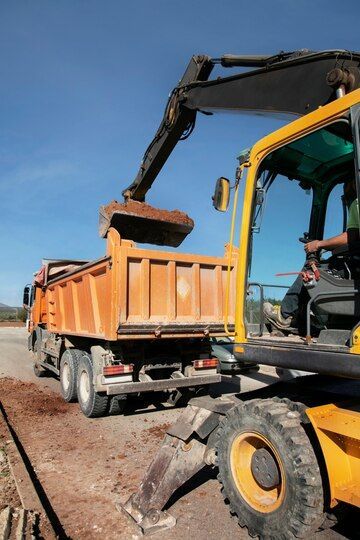 A Dump Truck is Being Loaded With Dirt by a Yellow Excavator — Andrew Johnston Haulage In Byron Bay, NSW