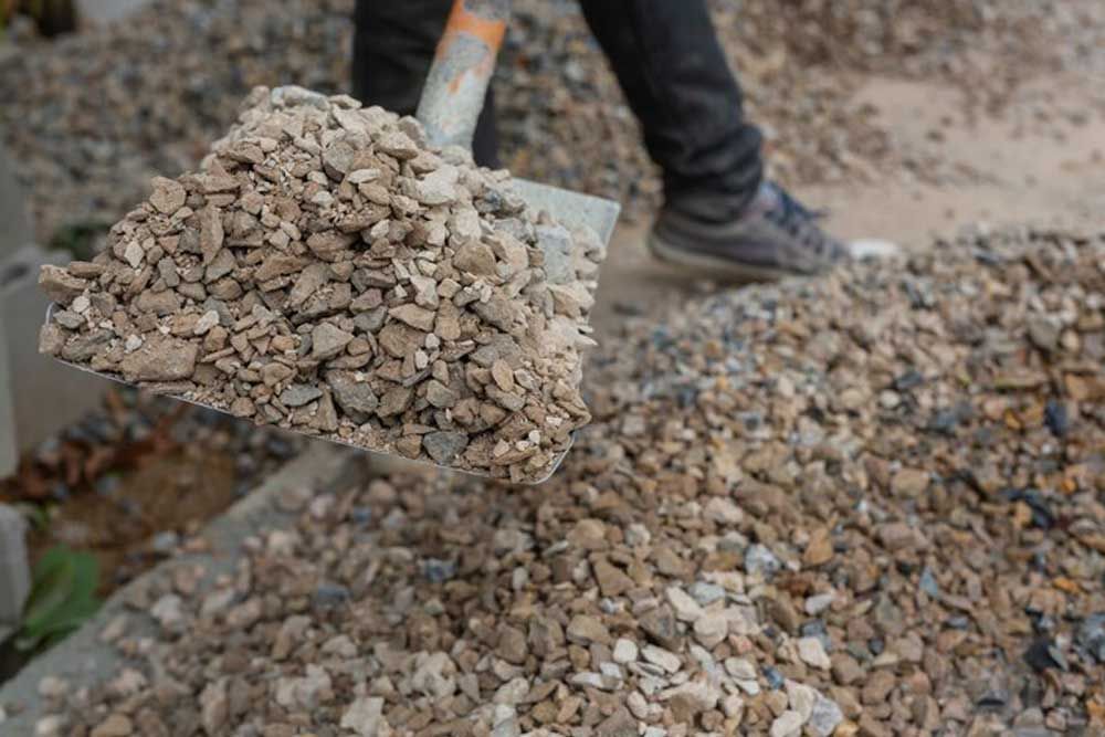 A Person Is Holding A Shovel Filled With Gravel — Andrew Johnston Haulage In Byron Bay, NSW