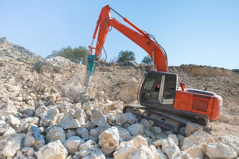 A Large Orange Excavator Is Working On A Pile Of Rocks — Andrew Johnston Haulage In Ballina, NSW