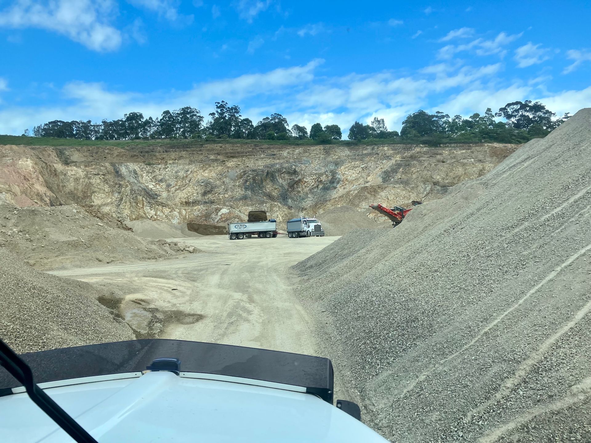 A Truck is Driving Down a Dirt Road Next to a Large Pile of Gravel — Andrew Johnston Haulage In Ewingsdale, NSW