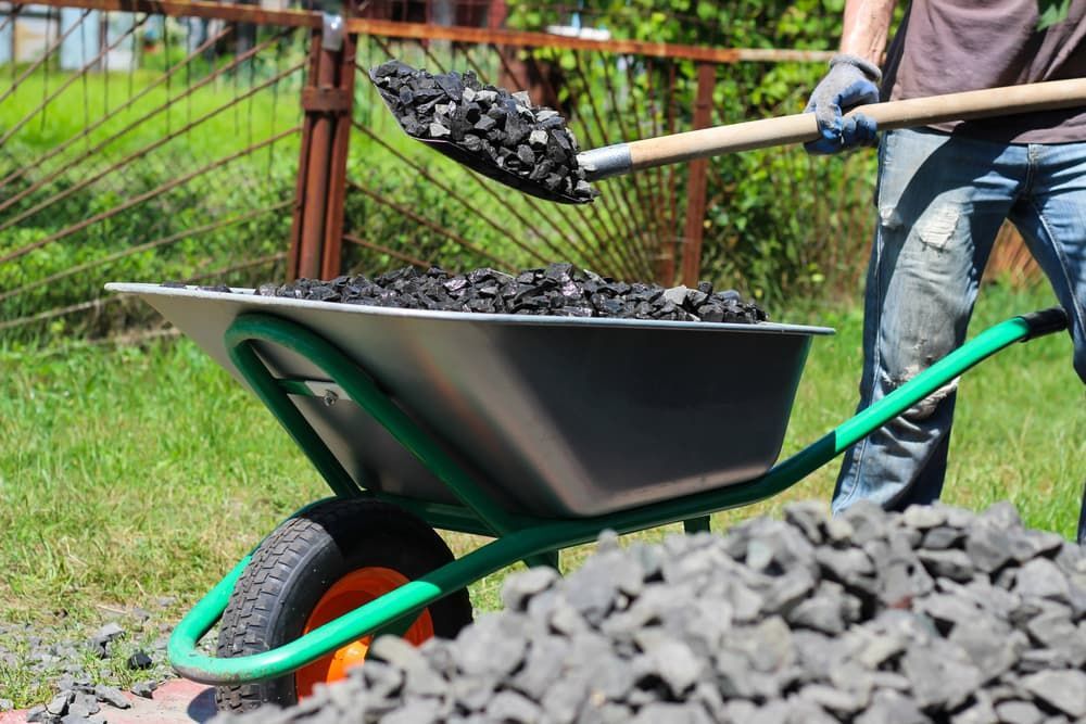 A Man Is Shovelling Coal Into A Wheelbarrow — Andrew Johnston Haulage In Gold Coast, QLD