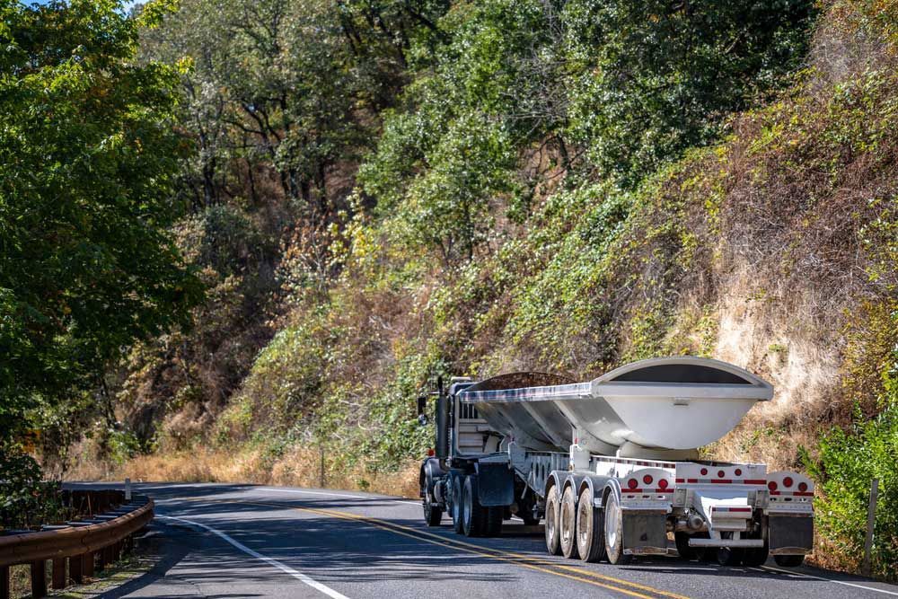 A Dump Truck Is Driving Down A Road With Trees On The Side — Andrew Johnston Haulage In Lismore, NSW