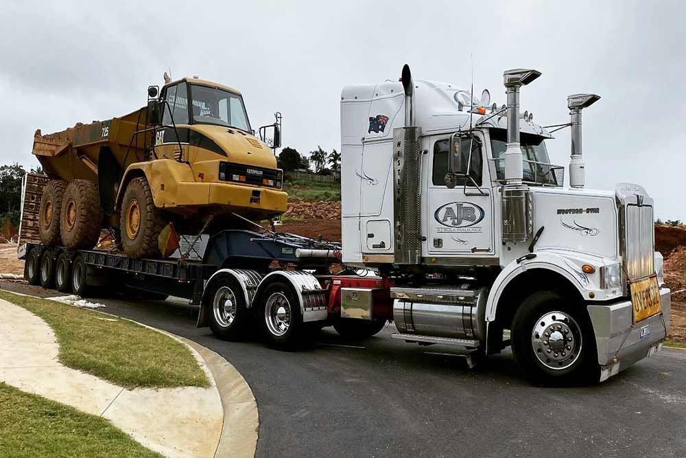 A White Semi Truck Carrying Yellow Tractor — Andrew Johnston Haulage In Gold Coast, QLD