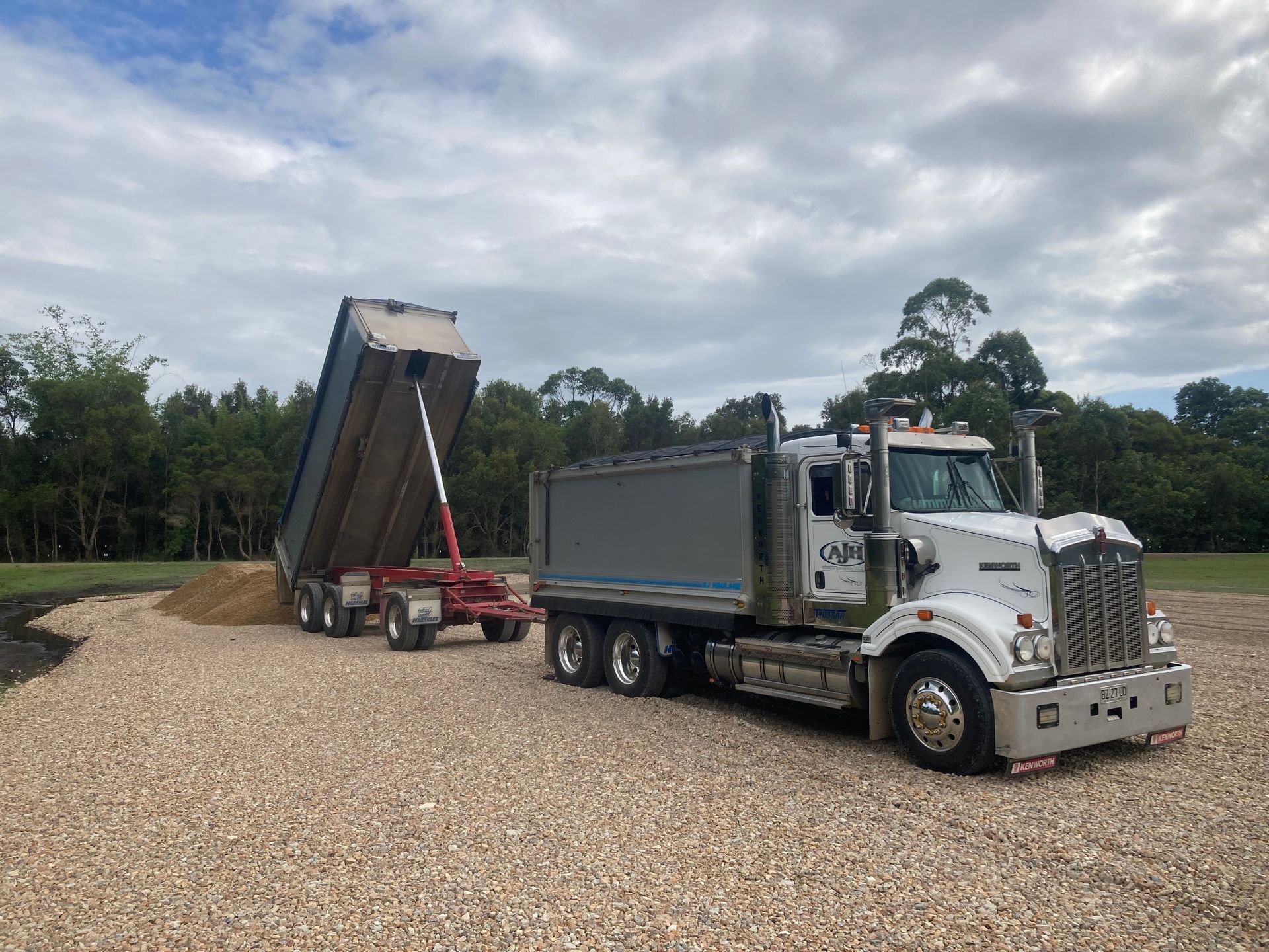 A Dump Truck is Parked in a Gravel Lot Next to a Trailer — Andrew Johnston Haulage In Ewingsdale, NSW