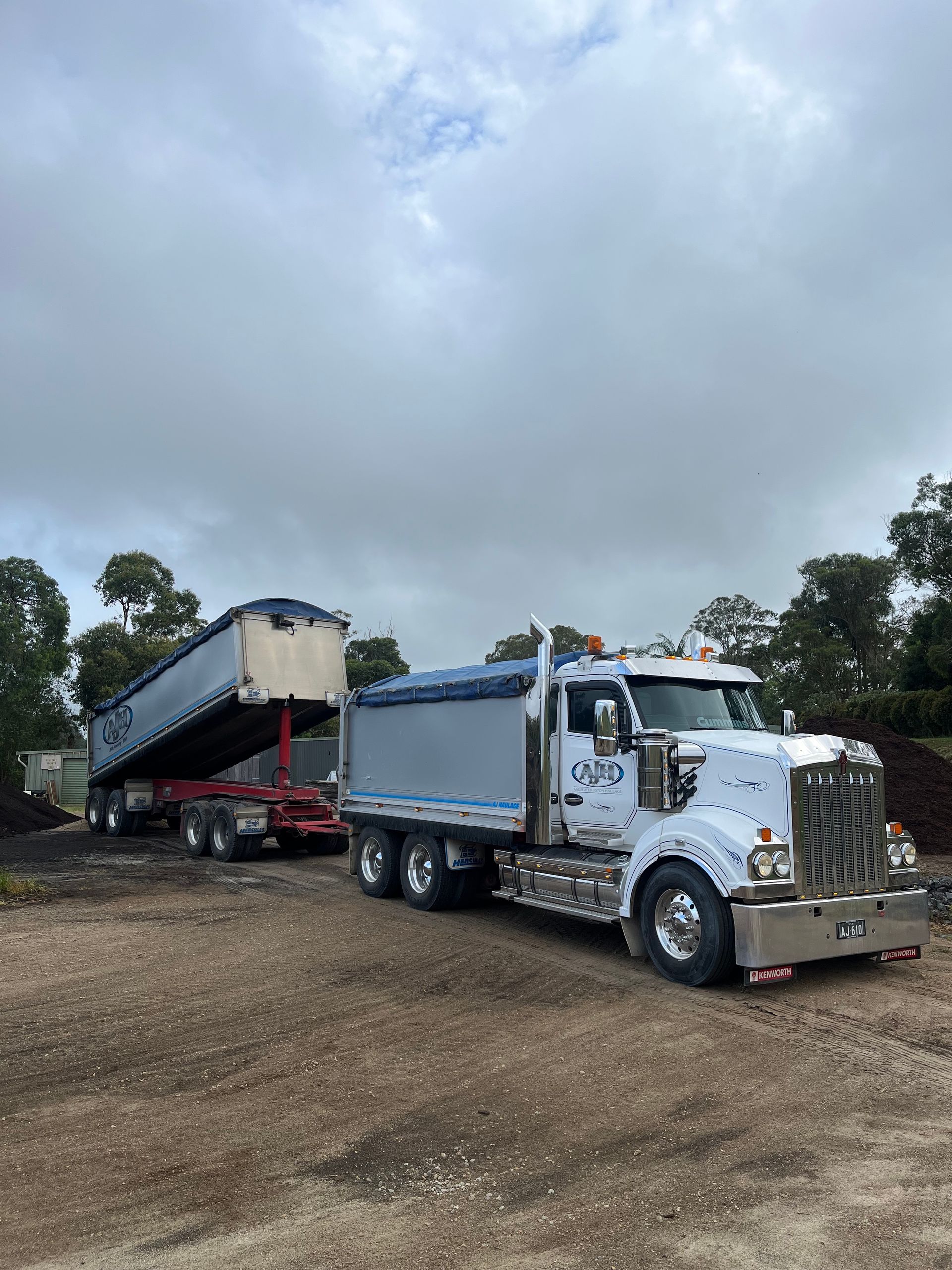 A Dump Truck With a Trailer Attached to It is Parked in a Dirt Lot — Andrew Johnston Haulage In Ewingsdale, NSW