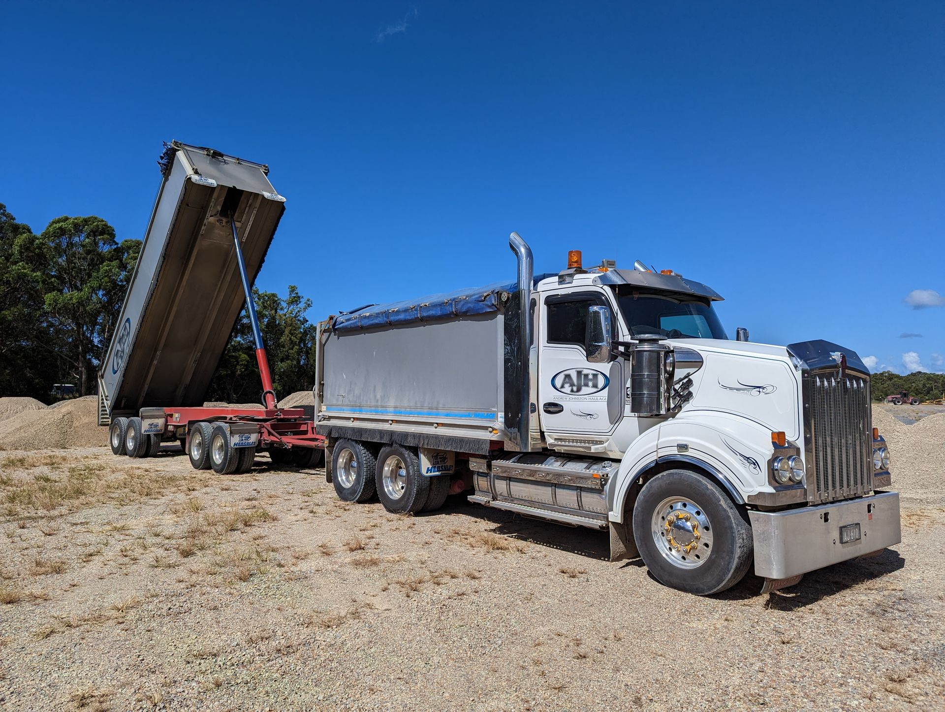 A Dump Truck With a Trailer Attached to It is Parked in a Dirt Field — Andrew Johnston Haulage In Ewingsdale, NSW