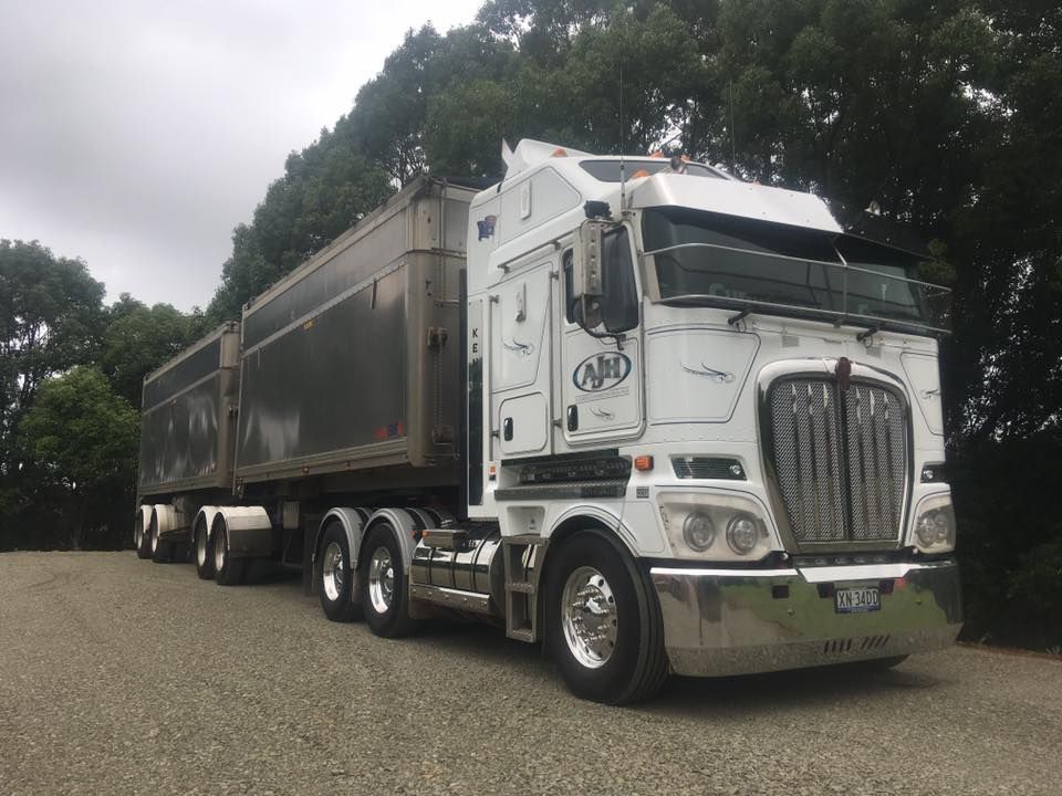 A White Semi Truck is Parked in a Gravel Lot Next to Trees  — Andrew Johnston Haulage In Ewingsdale, NSW