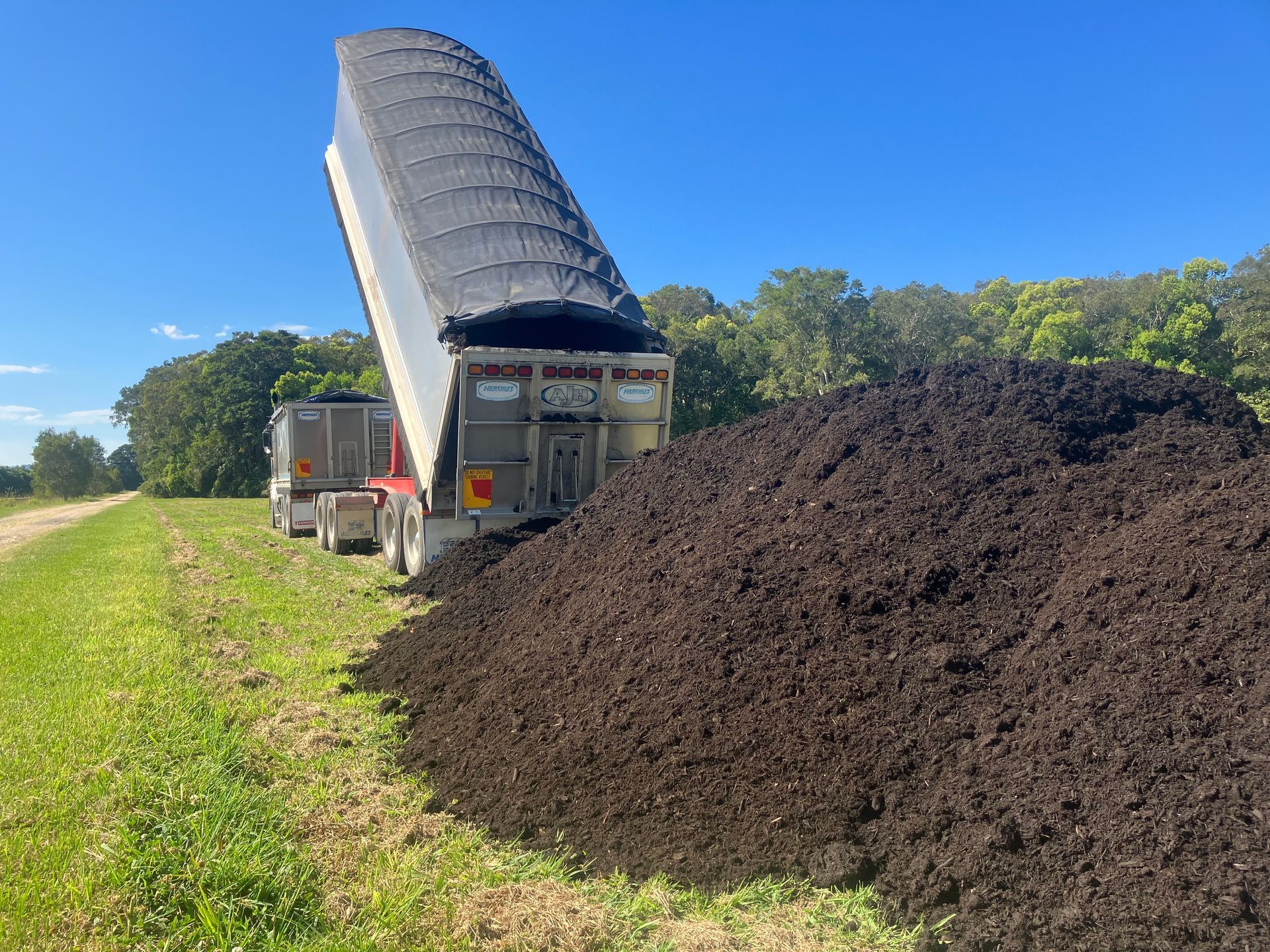 A Dump Truck is Dumping a Large Pile of Dirt Into a Field — Andrew Johnston Haulage In Ewingsdale, NSW