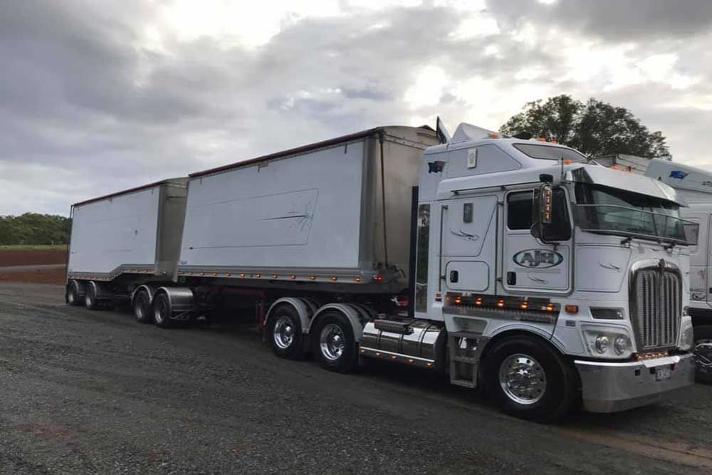A White Semi Truck With a Trailer Attached to It is Parked in a Parking Lot — Andrew Johnston Haulage In Grafton, NSW