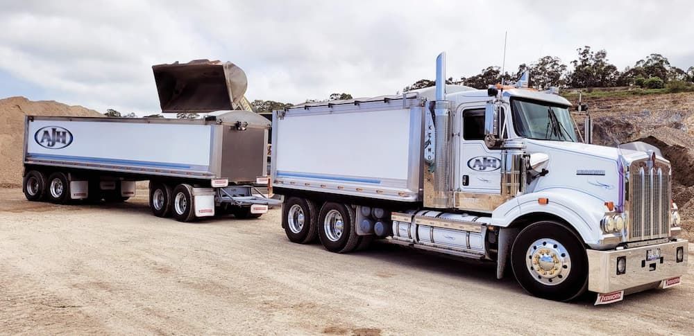 A Dump Truck With a Trailer Attached to It is Parked on a Dirt Road — Andrew Johnston Haulage In Ewingsdale, NSW