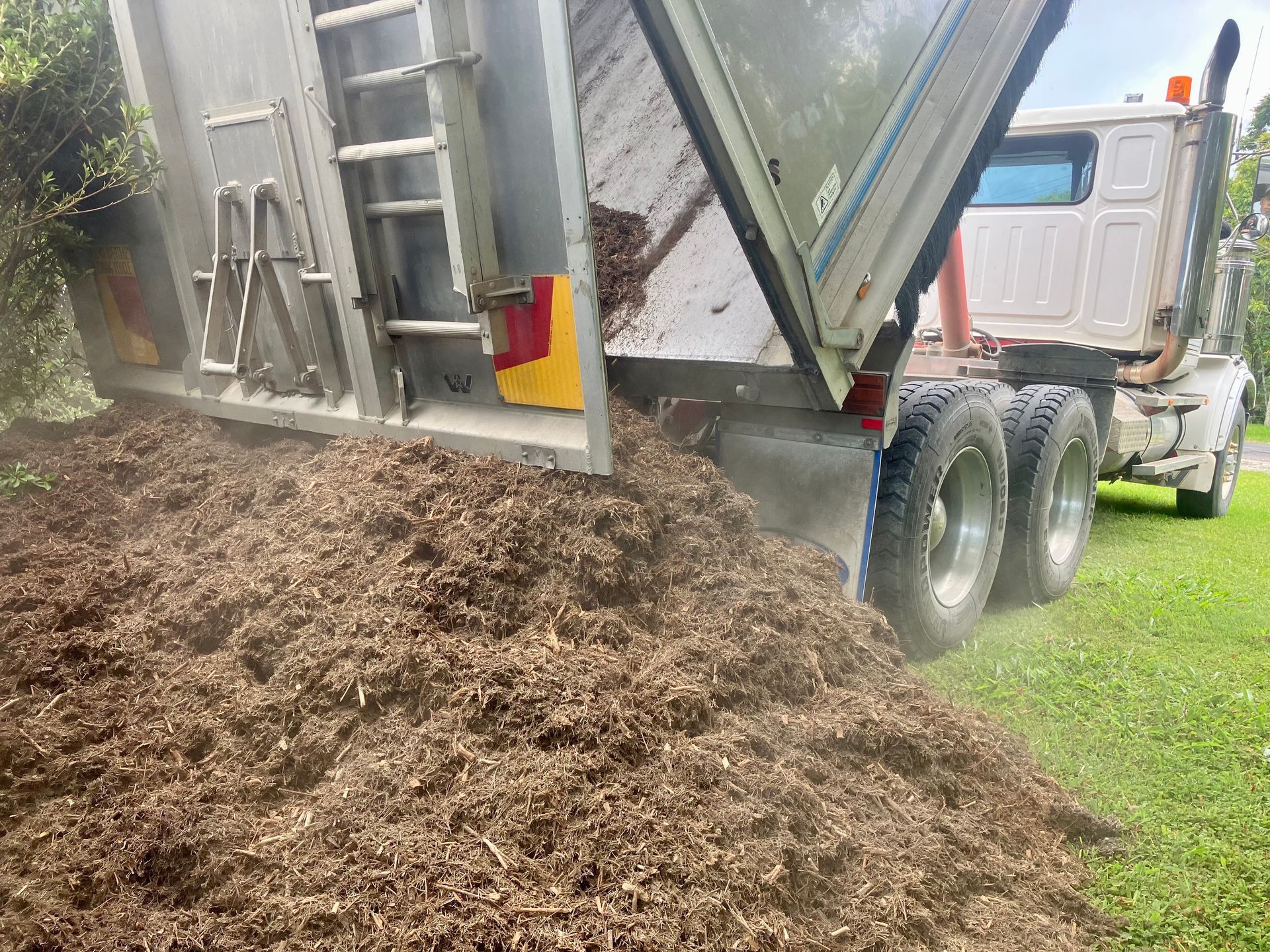 A Dump Truck is Dumping a Pile of Mulch Into the Grass