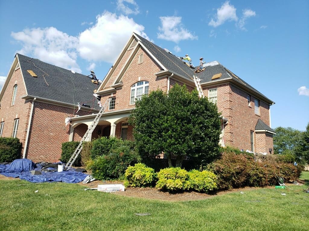 Brick suburban house with gabled roof, front porch, and landscaped lawn under a blue sky