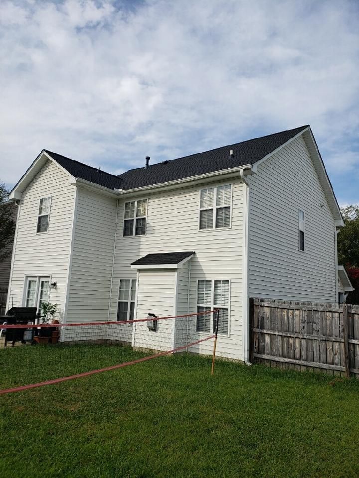 Two-story white house with black roof and fenced backyard under a cloudy sky.