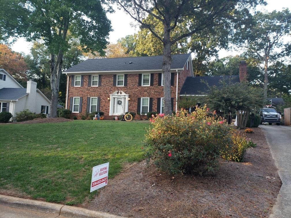 Brick two-story house with white trim, front lawn, shrubs, and a driveway in a leafy neighborhood.