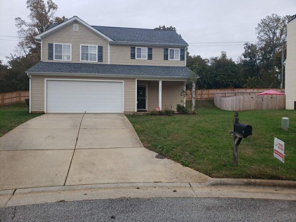 Suburban two-story house with white garage, driveway, front lawn, and a mailbox by the curb