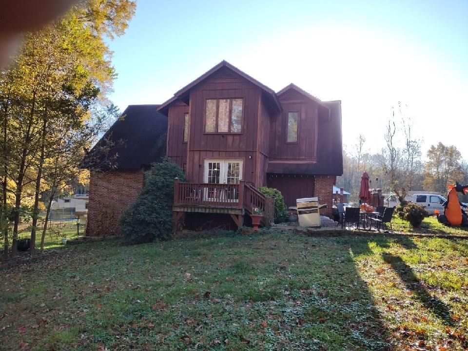 Two-story brown house with a small porch and leaf-covered yard in autumn sunlight