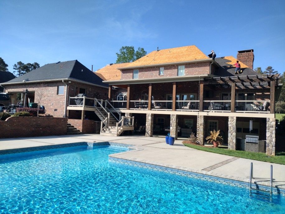 Backyard with a blue swimming pool in front of a brick house with a covered patio and stairs