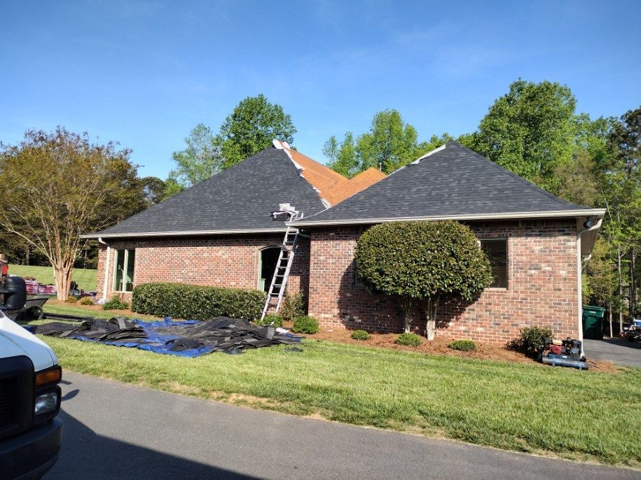 Brick suburban house with dark roof, trimmed bushes, and a manicured lawn on a sunny day