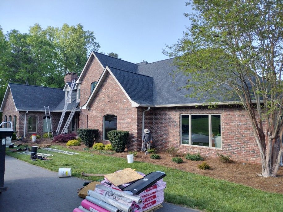 Brick house with dark roof and large windows, front yard under construction with stacked materials.