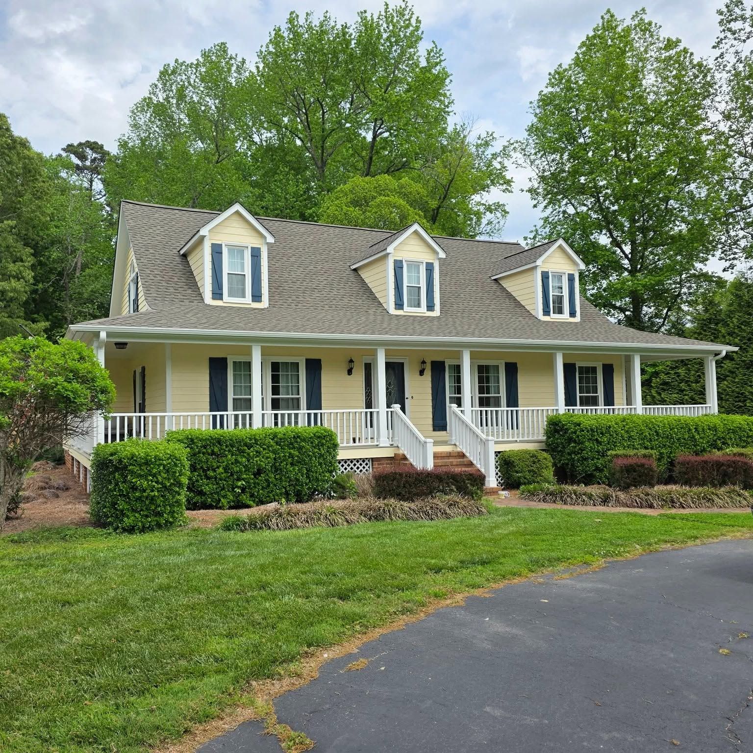 Yellow two-story house with white trim, porch, dormer windows, and a curved driveway in front