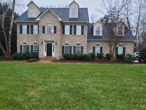 Large two-story stone house with black shutters and a spacious green lawn