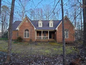 Brick house with a covered porch, dormer windows, and trees in the front yard