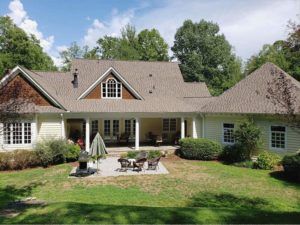 Suburban house with a covered porch, patio furniture, and a green lawn surrounded by trees