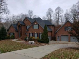 Brick suburban house with gray roof, two-car garage, and a curved driveway on a cloudy day