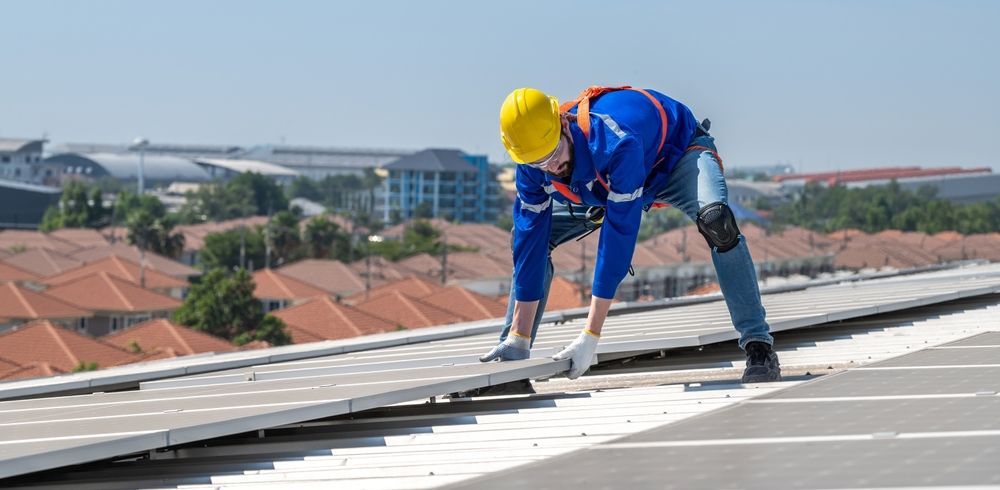 Worker in blue safety gear and yellow helmet installing rooftop panels on a building.