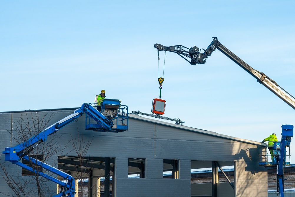 Construction workers on blue lifts repairing a gray building roof under a clear sky