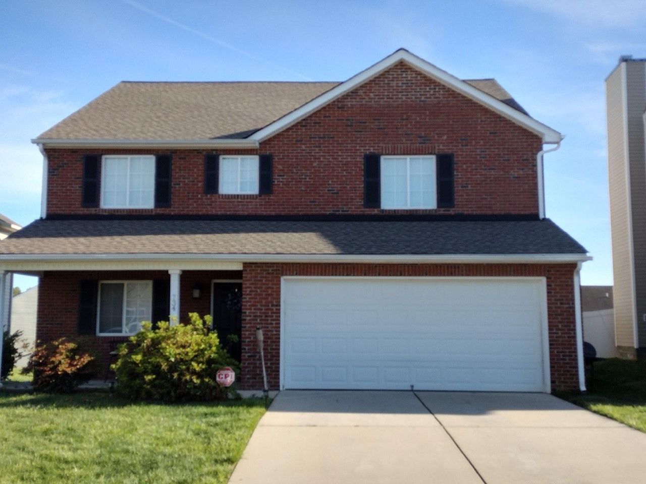 Two-story brick suburban house with white garage and front porch under a clear blue sky