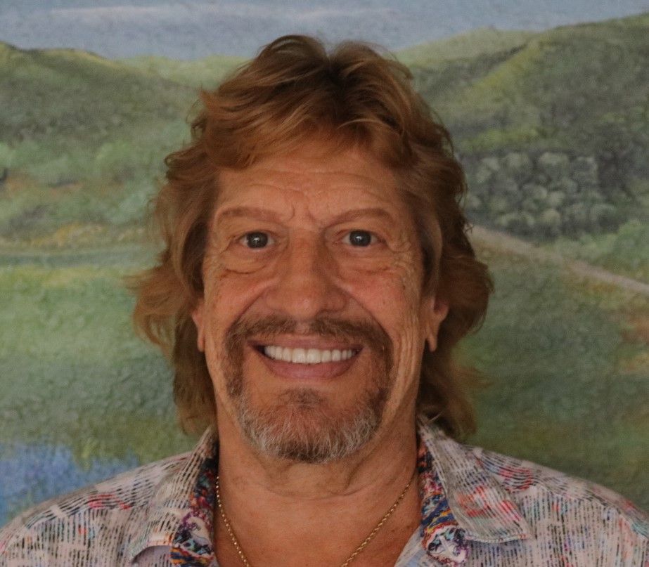 Smiling man in a green shirt beside a lit aquarium with fish and plants