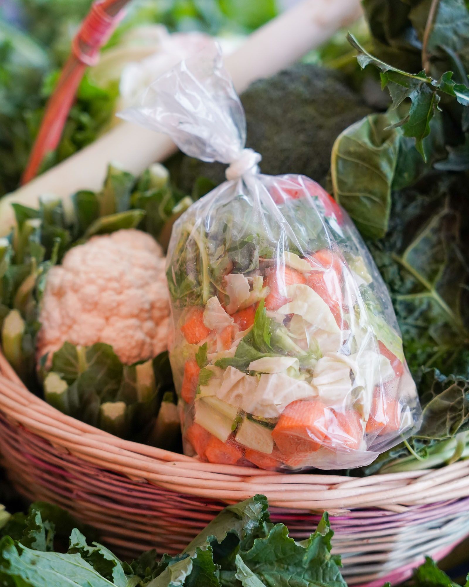 Cesto di verdure fresche, tra cui carote e broccoli, con un sacchetto di verdure pretagliate.