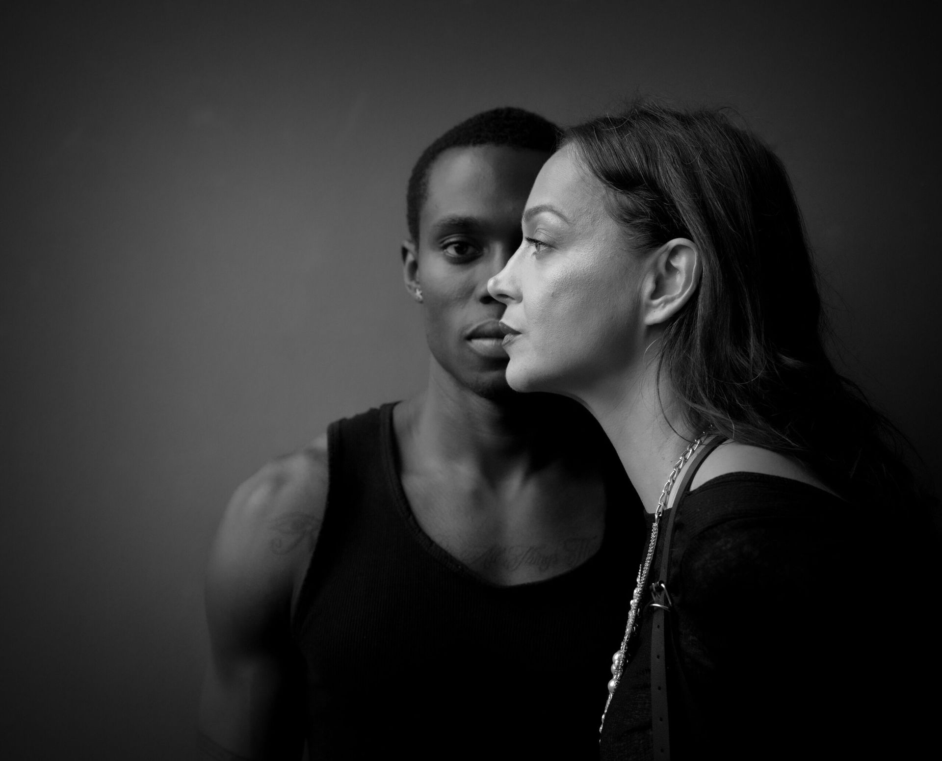 Photo en noir et blanc d'un homme et d'une femme. La femme se penche vers lui ; ils partagent le même espace. Fond sombre.