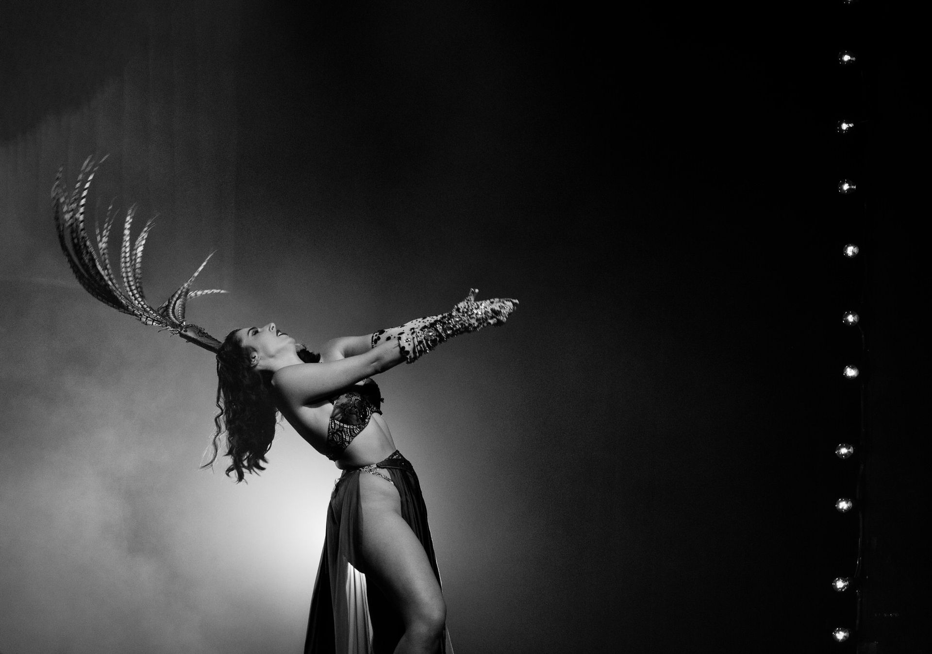 Une danseuse en costume à plumes, les bras levés, se produisant sur scène.