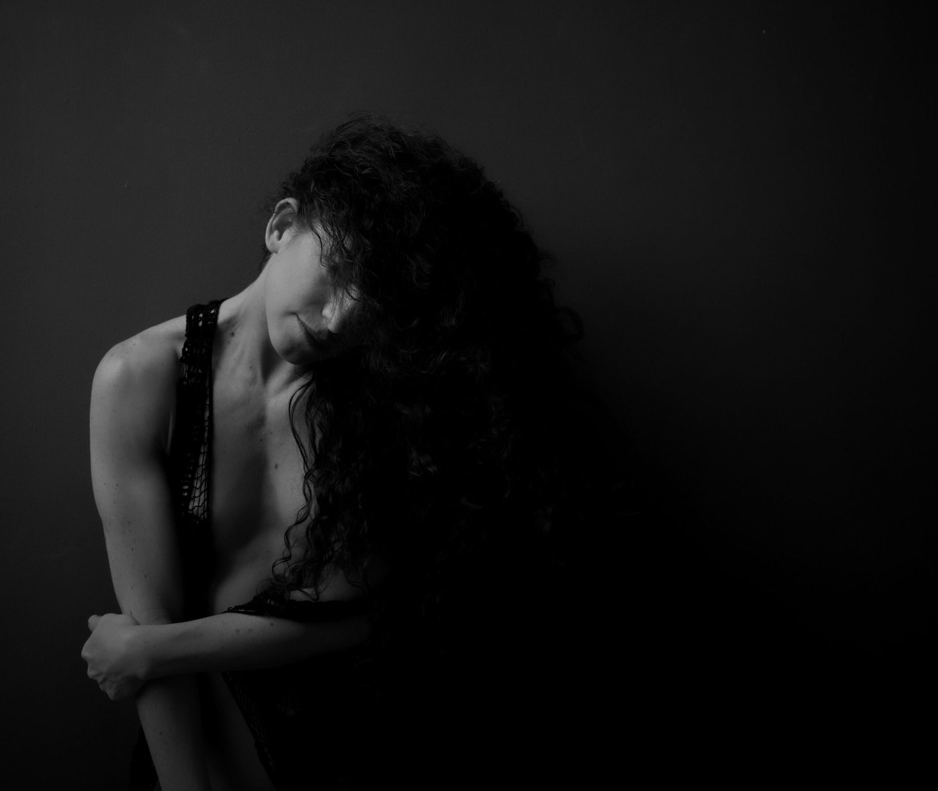 Femme, tête inclinée, bras croisés. Cheveux noirs et bouclés en cascade. Photo en noir et blanc.