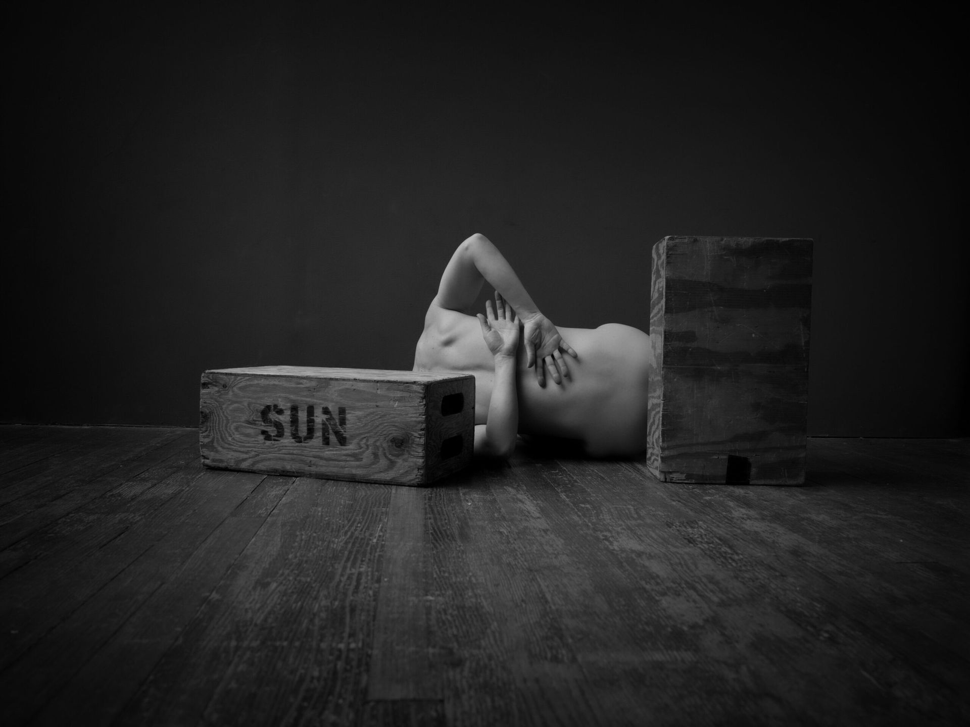 Personne nue allongée sur le sol, partiellement dissimulée par des briques ; sur une brique, on peut lire « SOLEIL » dans un décor sombre.