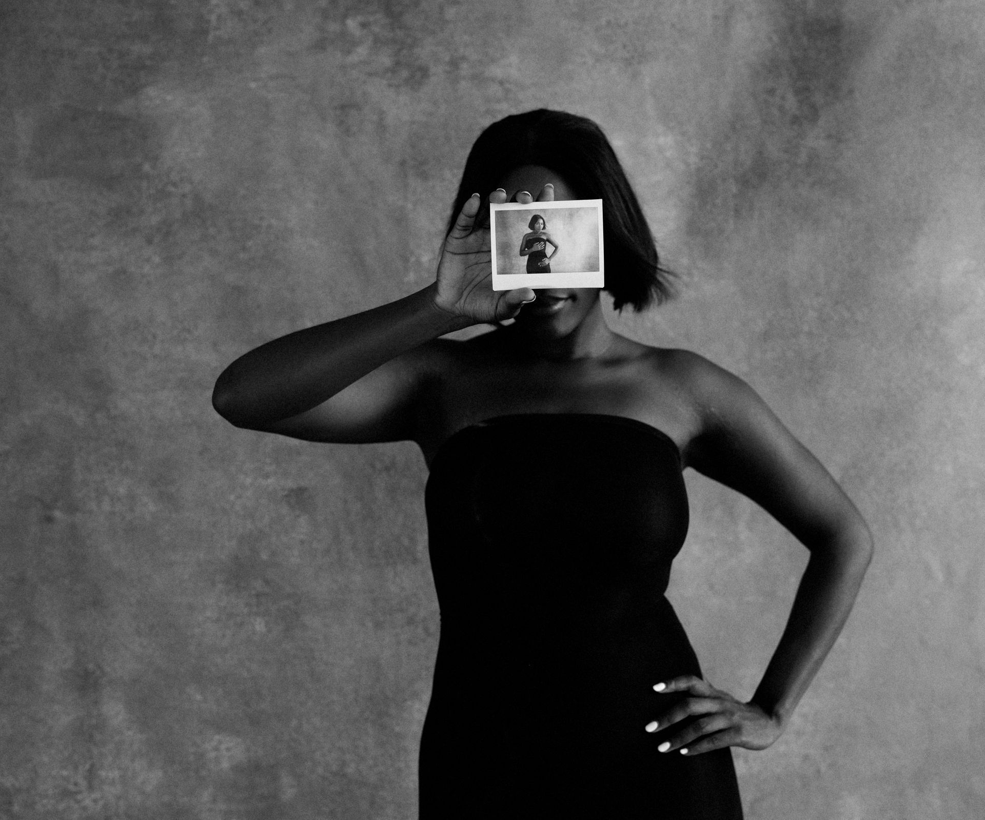 Femme en chemise blanche regardant hors champ, main dans les cheveux, fond noir.