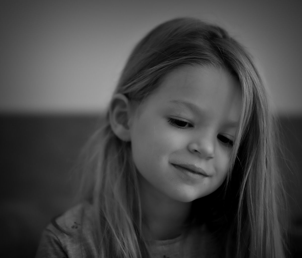 Jeune fille aux longs cheveux, le regard baissé, esquissant un sourire. Photo en noir et blanc.