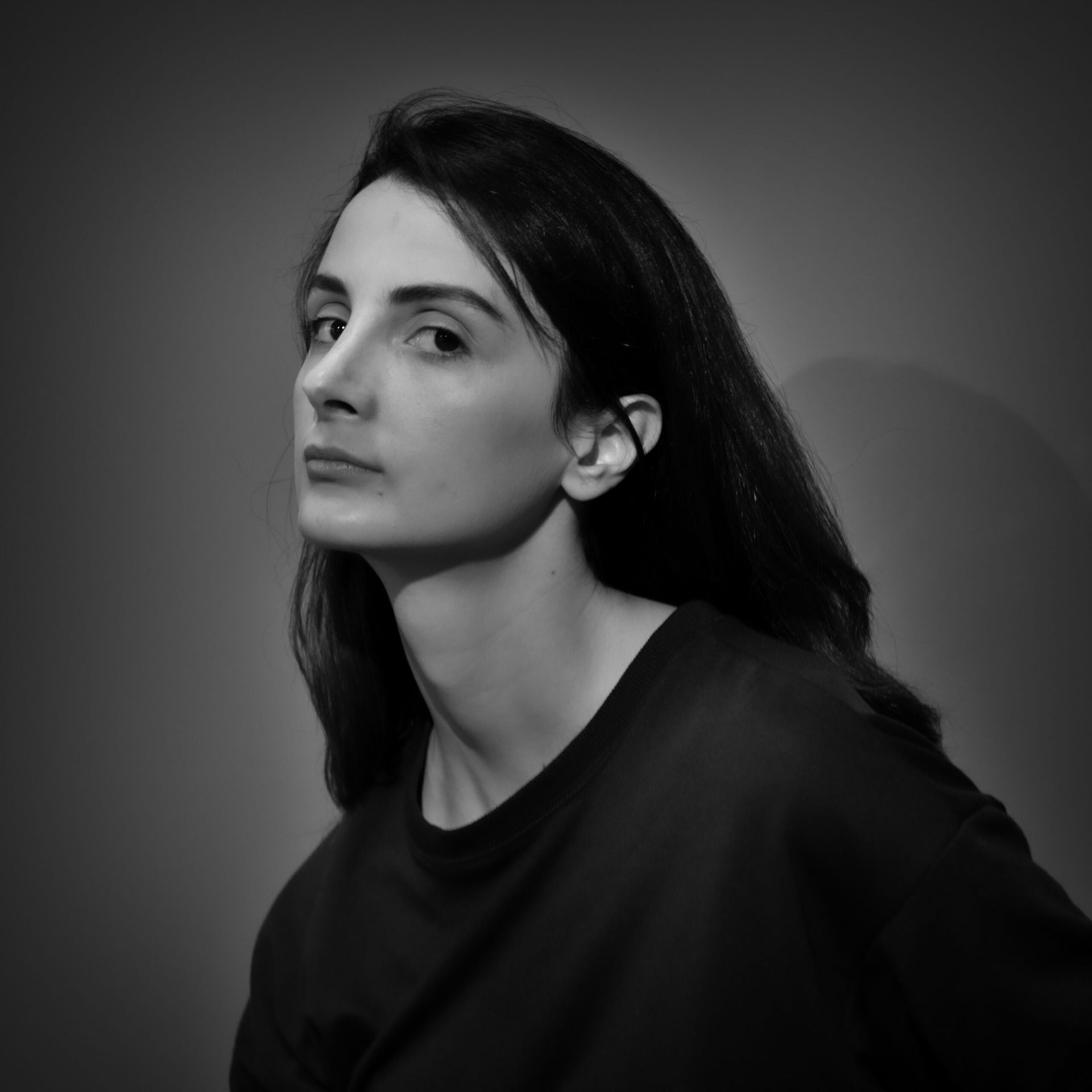 Femme aux longs cheveux noirs, regardant l'objectif, vêtue d'un haut foncé, sur fond gris.