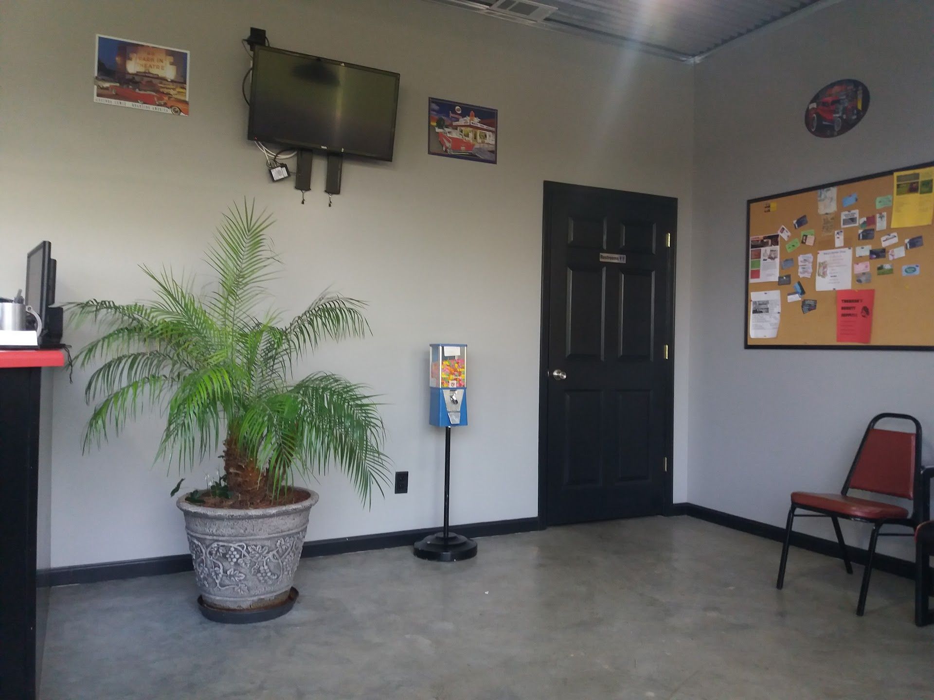 Waiting room with TV, potted plant, black door, bulletin board, and chairs. | Complete Car Care Auto Sales & Service