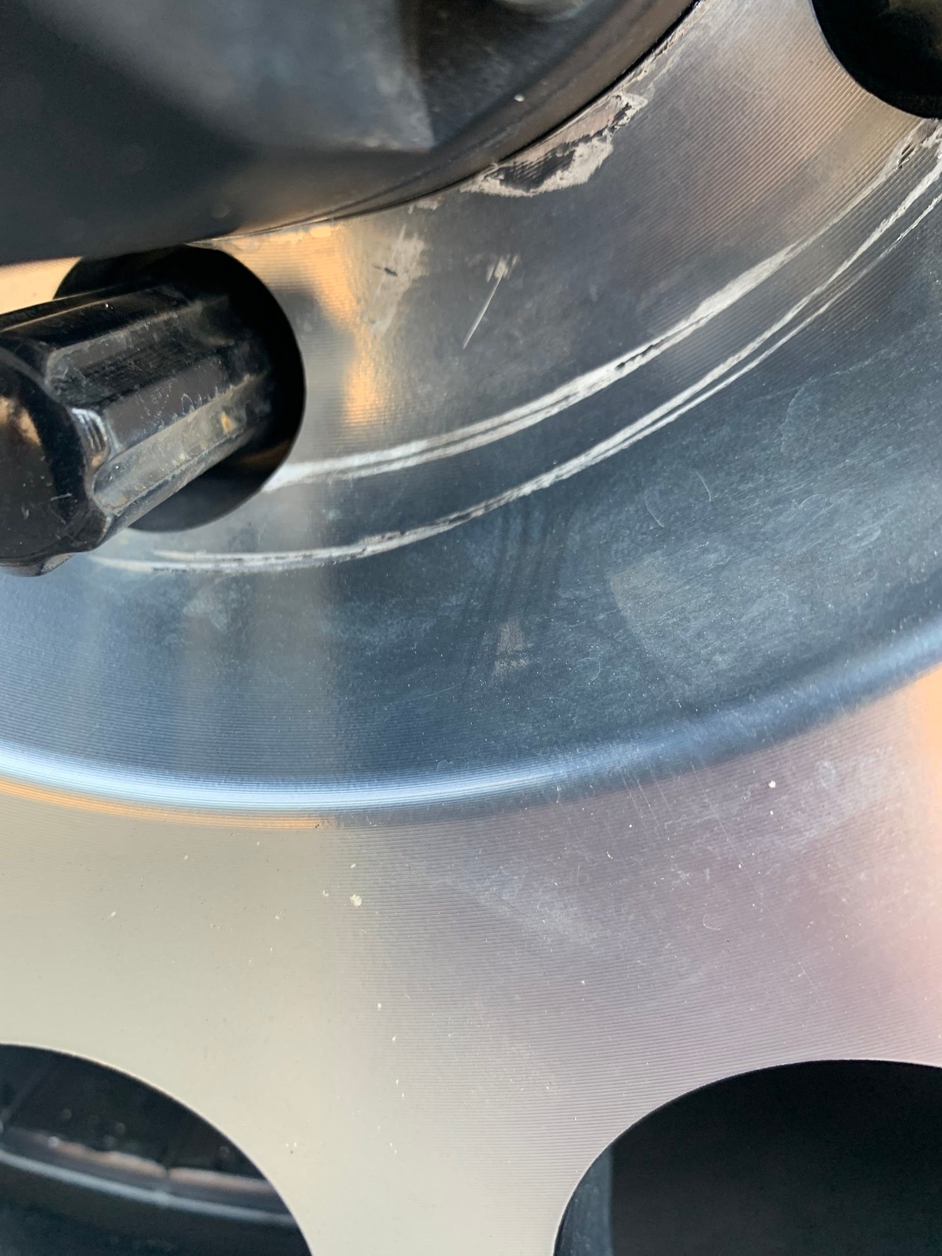 Close-up of a silver metal wheel rim with black lug nuts and circular cutouts | Complete Car Care Auto Sales & Service