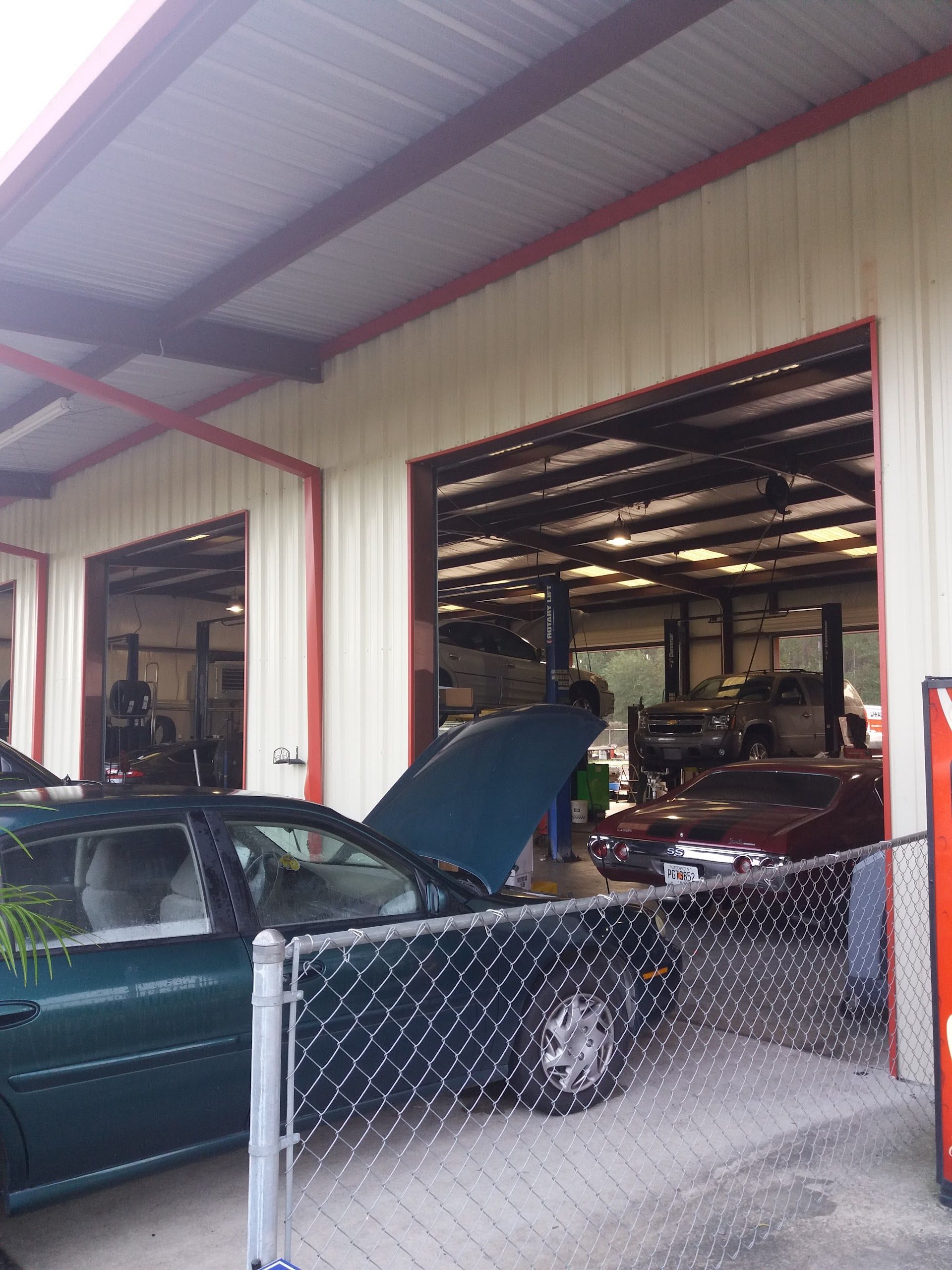 Garage with a green car, hood open, parked behind a chain-link fence inside an auto shop | Complete Car Care Auto Sales & Service