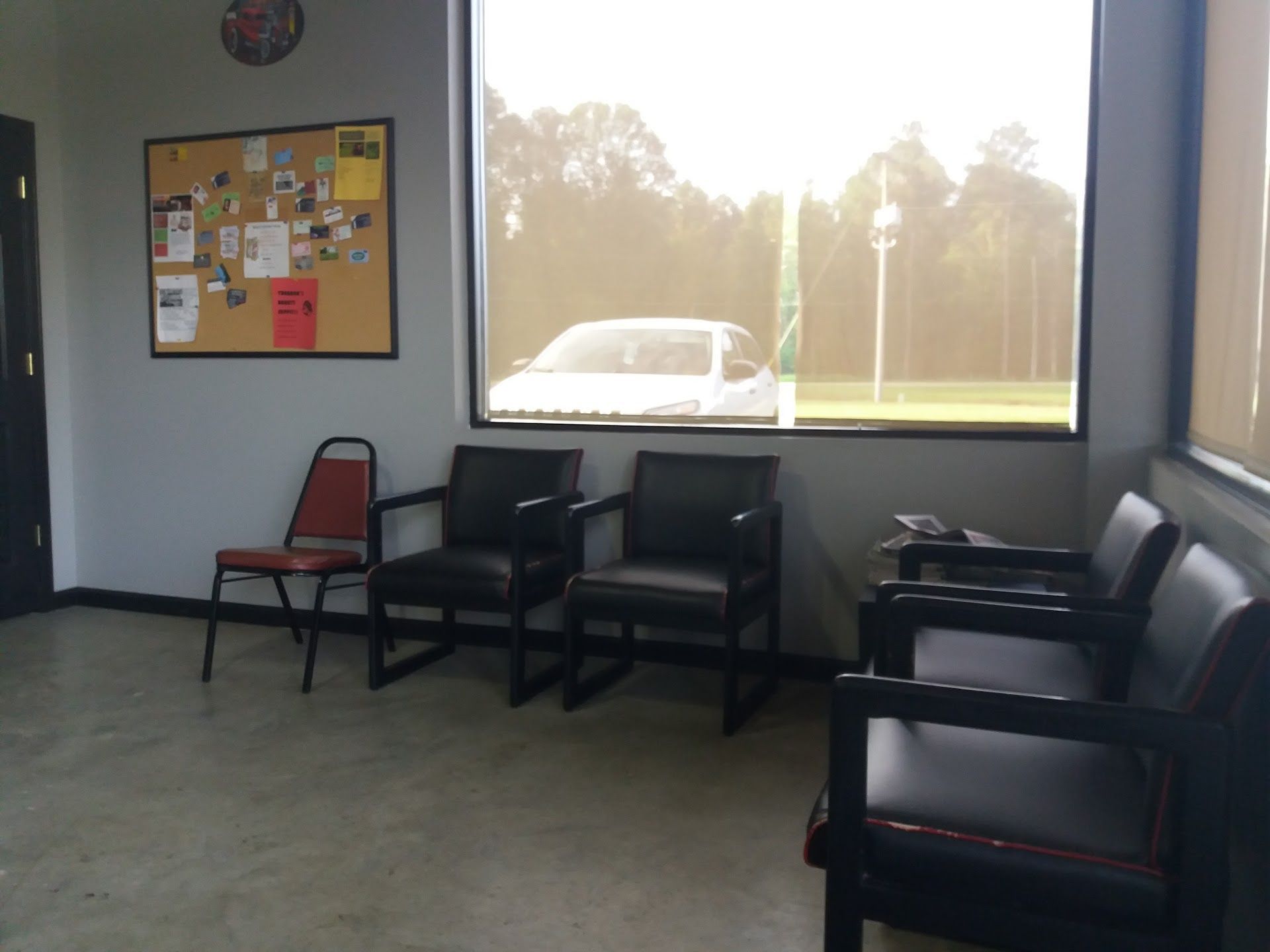 Waiting room with black chairs, a red chair, bulletin board, and bright window view outside. | Complete Car Care Auto Sales & Service