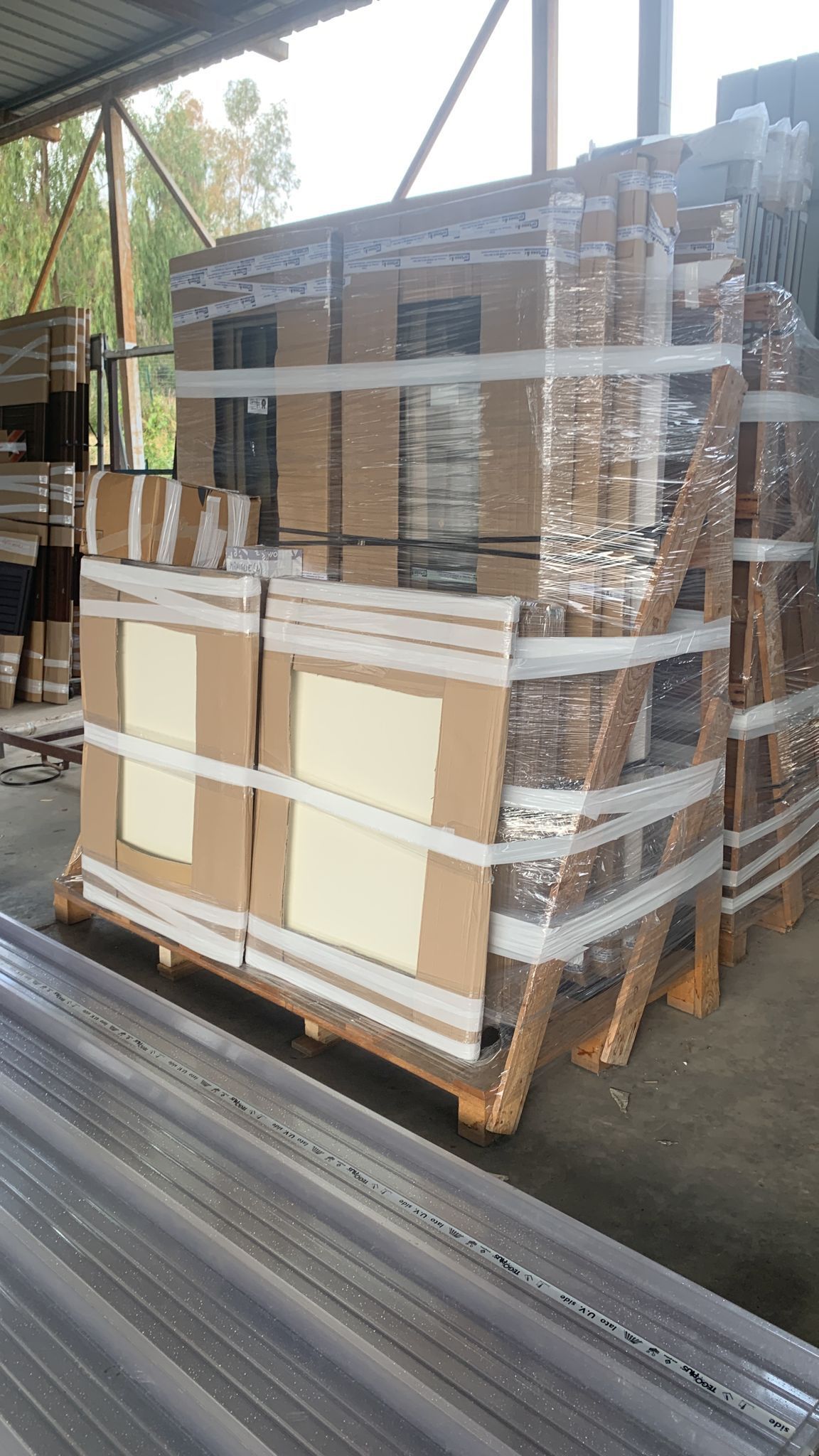 Pallet di merci imballate e avvolte nella plastica sul pavimento di un magazzino, con pannelli di cartone impilati davanti.