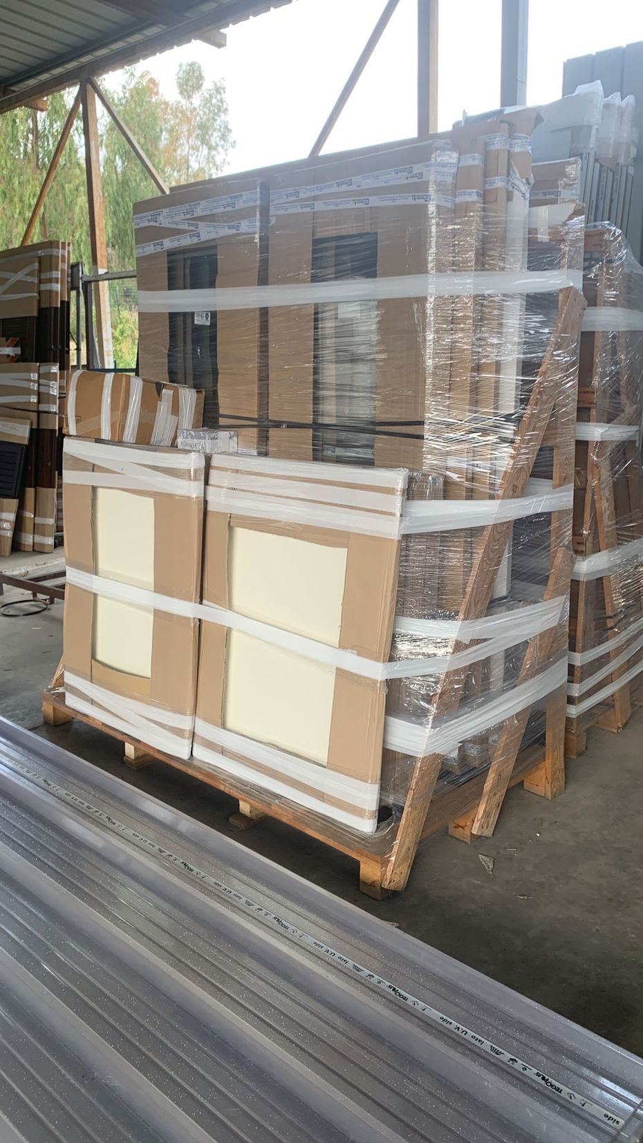 Pallet di merci imballate e avvolte nella plastica sul pavimento di un magazzino, con pannelli di cartone impilati davanti.