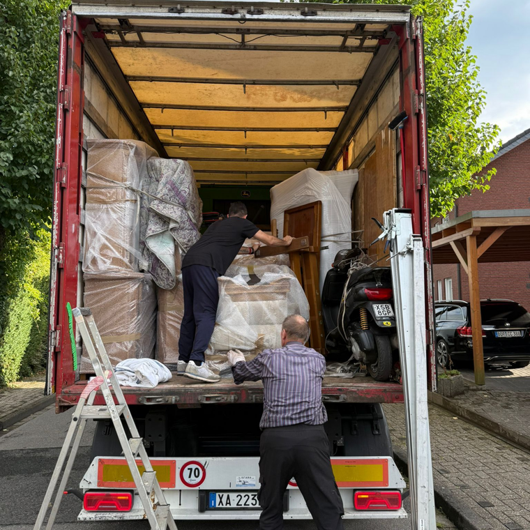 Due traslocatori scaricano mobili imballati da un camion rosso in un vialetto, con una motocicletta all'interno.