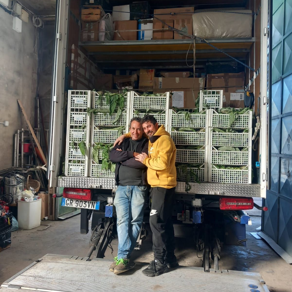 Due persone sorridono all'interno di un camion carico di casse bianche impilate, all'interno di un magazzino.