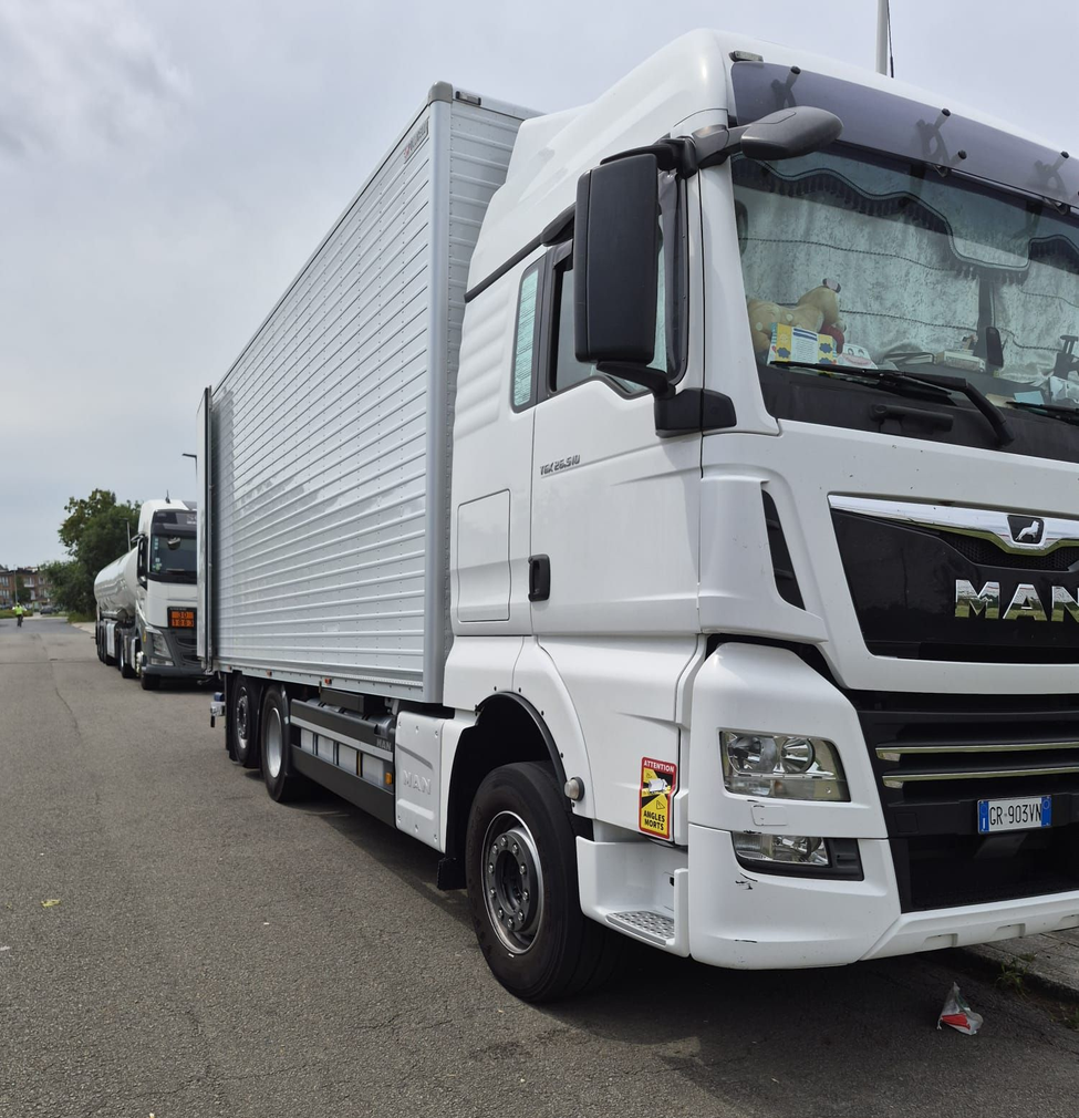 Un furgone bianco parcheggiato su una strada, con un altro camion alle sue spalle, sotto un cielo nuvoloso.